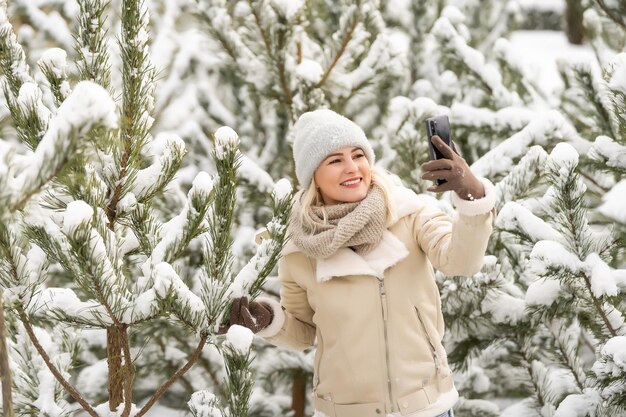 la donna si fa un selfie nella foresta innevata durante un'avventura invernale. donna tra i pini