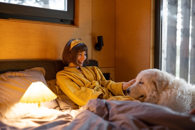 La donna si prende cura del suo cane mentre giace a letto nella piccola camera da letto della cabina di legno sulla natura