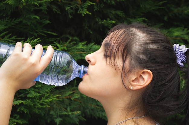 La donna si prende una breve pausa e beve acqua durante l'allenamento nel parco