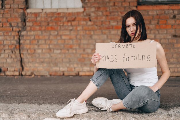 La donna si siede con un poster Prevenire la carestia di massa Donna con sguardo triste devastato guarda nella fotocamera