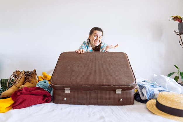 La donna si siede sul letto con la valigia e i vestiti intorno al concetto di viaggio decide il paese caldo o freddo dove andare