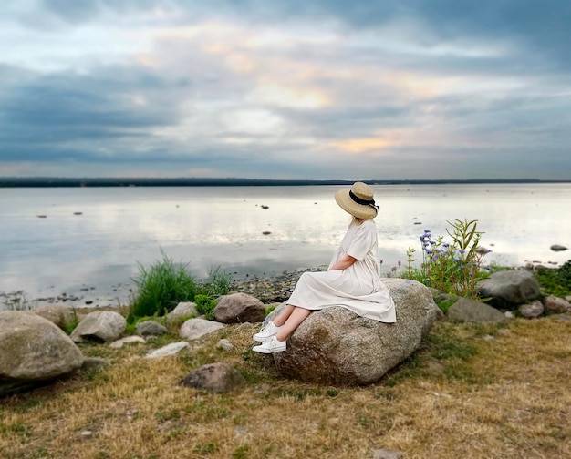 la donna si siede sulla pietra sulla spiaggia selvaggia e guarda il cielo nuvoloso dopo la tempesta