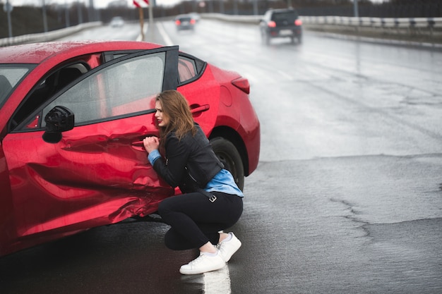 La donna si siede vicino a un'auto rotta dopo un incidente. chiamare per aiuto. assicurazione auto