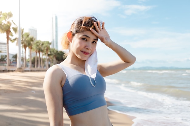 La donna si toglie la maschera e si riposa dopo aver finito di fare jogging sulla spiaggia in estate