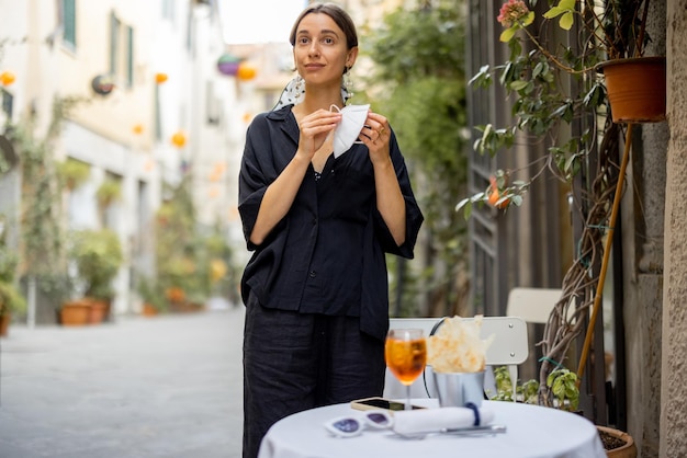 La donna si toglie la maschera mentre è seduta al ristorante italiano all'aperto