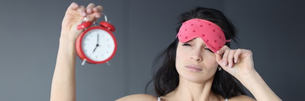 La donna si toglie la maschera per dormire e guarda la sveglia