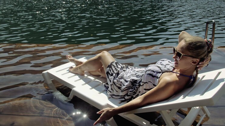 Foto la donna si trova su un lettino con occhiali da sole e uno scialle di seta boho la ragazza riposa su un molo sottomarino di legno inondato il marciapiede è coperto di acqua nel lago
