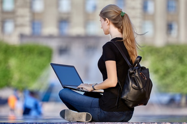 La donna snella nella sua s lavora a distanza per strada usando il laptop