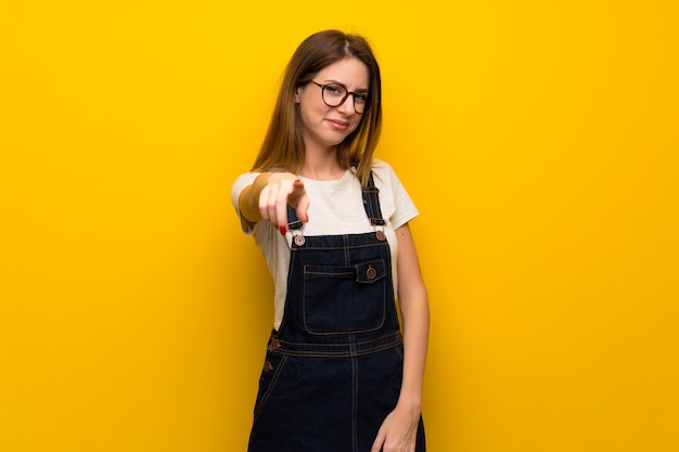 La donna sopra il muro giallo punta il dito contro di te con un&#39;espressione fiduciosa