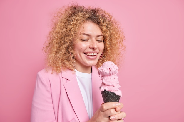 La donna sorride ampiamente andando a mangiare un gustoso cono gelato alla fragola in waffle boost mood con deliziosi snack pone su roseo