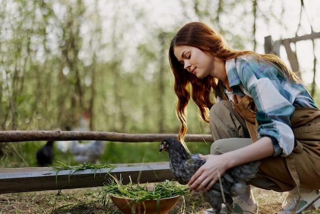 La donna sorride guardando il pollo che tiene vicino alla mangiatoia nelle sue mani nella fattoria lavoro agricolo per allevare uccelli sani e dar loro da mangiare cibo biologico in natura