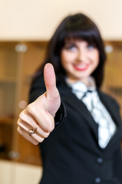 La donna sorridente attraente in ufficio mostra il pollice su, ficus su un dito