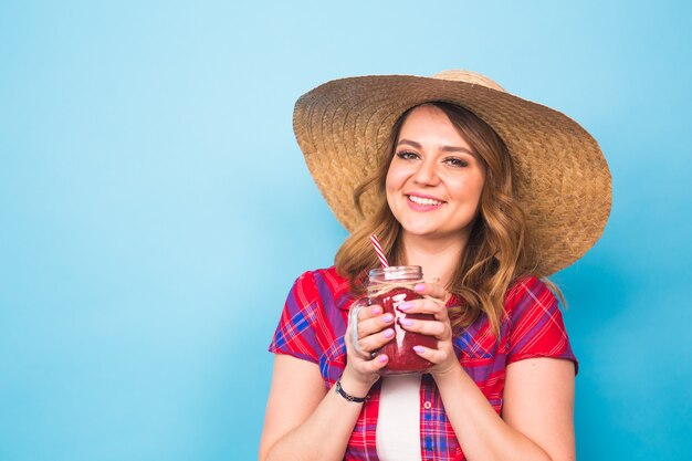 La donna sorridente beve il succo rosso. ritratto in studio con sfondo blu e copia spazio.