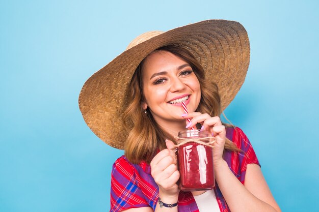 La donna sorridente beve il succo rosso. ritratto in studio con sfondo blu e copia spazio.