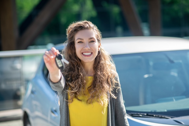 La donna sorridente con l'automobile digita la mano tesa