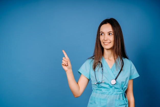 La donna sorridente del medico nello stetoscopio mostra qualcosa. Isolato su sfondo blu.