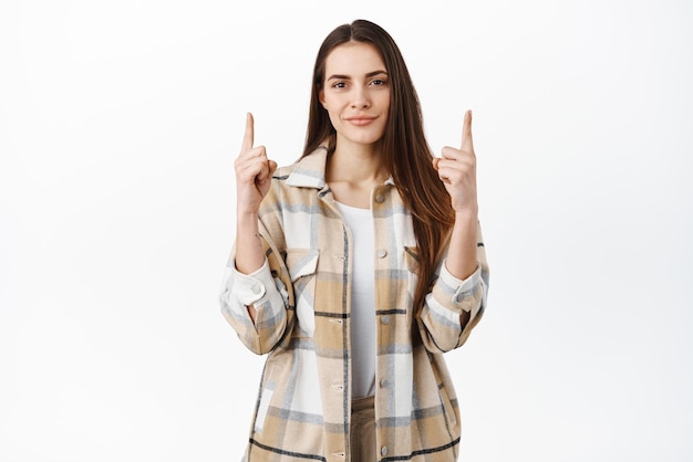 La donna sorridente e sicura di sé dà una raccomandazione puntando il dito verso l'alto e guardando lode determinato un buon affare mostra che la pubblicità sta su sfondo bianco