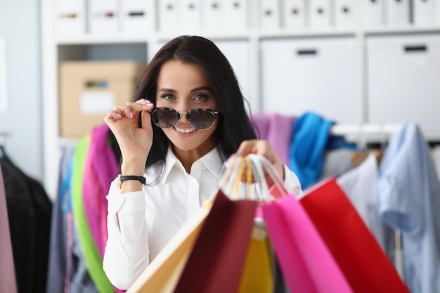 La donna sorridente felice dello shopping porta pacchi con vestiti femminili che tengono molti pacchi