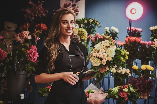 La donna sorridente felice sta lavorando al mazzo come fiorista al negozio di fiori.