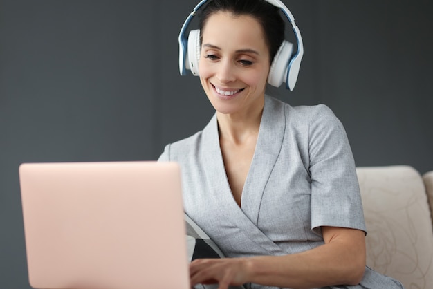 La donna sorridente in cuffie lavora dietro il computer portatile. Concetto di lavoro a distanza