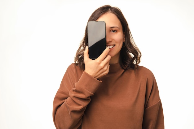 La donna sorridente nasconde metà del suo viso dietro il telefono mentre mostra il suo schermo