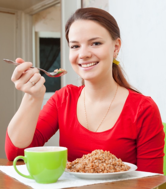 La donna sorridente nel rosso mangia il porridge del grano saraceno