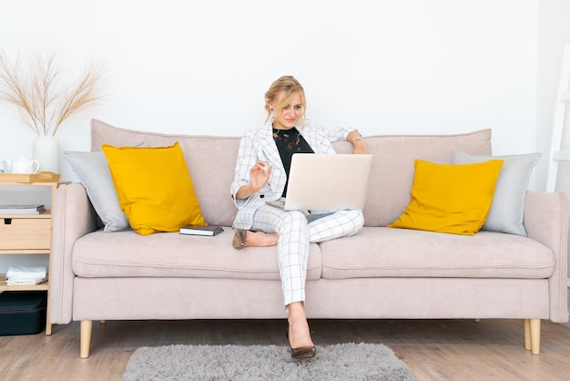 La donna sorridente si siede sul sofà che guarda il webinar sul computer portatile giovane donna felice in uso