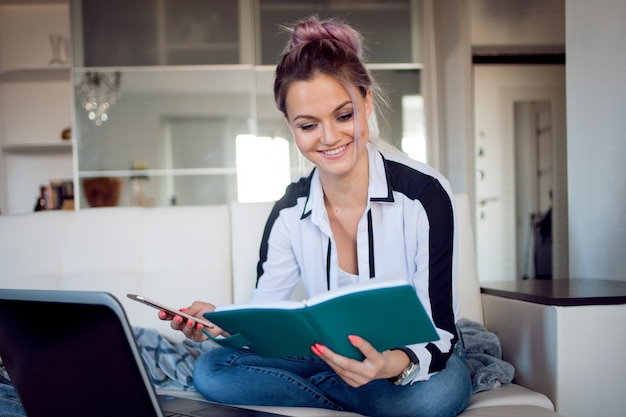 La donna sorridente tiene il suo pianificatore. Bella ragazza che lavora a casa con il computer portatile. blogger o studente freelance