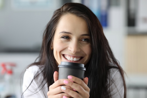 La donna sorridente tiene la tazza di carta nera