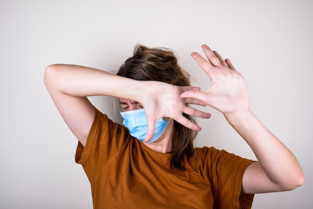 La donna spaventata nella mascherina medica copre il viso con le mani, isolate