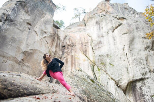 La donna sportiva adatta sta praticando lo yoga sul masso nella natura