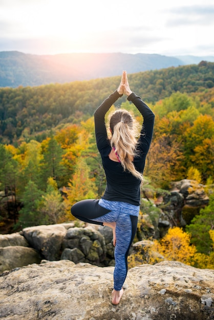 La donna sportiva adatta sta praticando lo yoga sulla cima della montagna