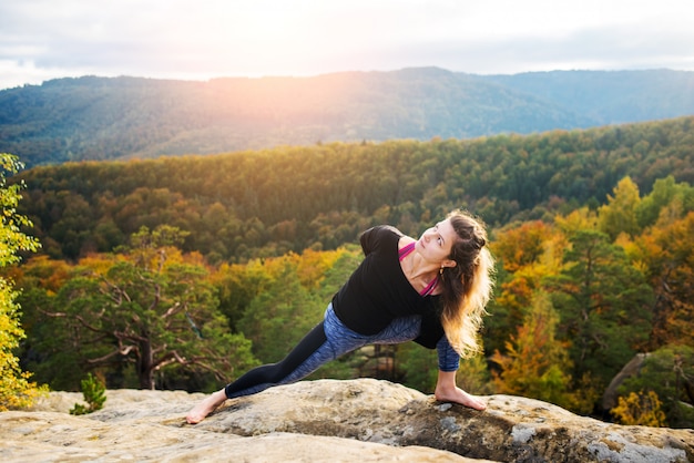 La donna sportiva adatta sta praticando lo yoga sulla cima della montagna