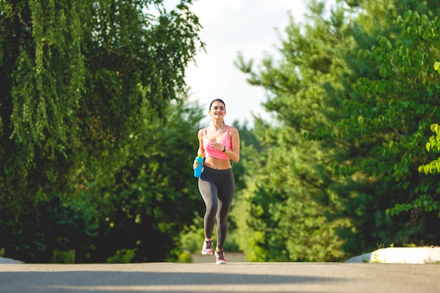 La donna sportiva che corre con una bottiglia all'aperto