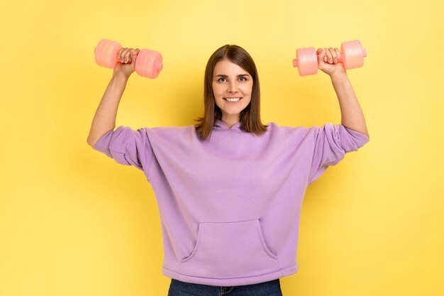 La donna sportiva ha alzato le braccia facendo esercizi di fitness con i manubri rosa che si allenano le mani