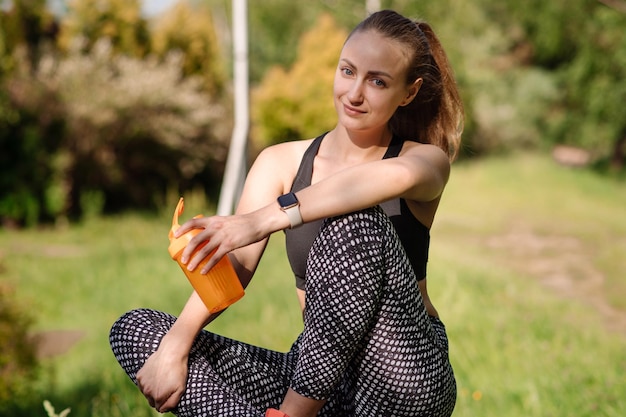 La donna sportiva in forma con la bottiglia d'acqua si rilassa dopo gli allenamenti all'aperto