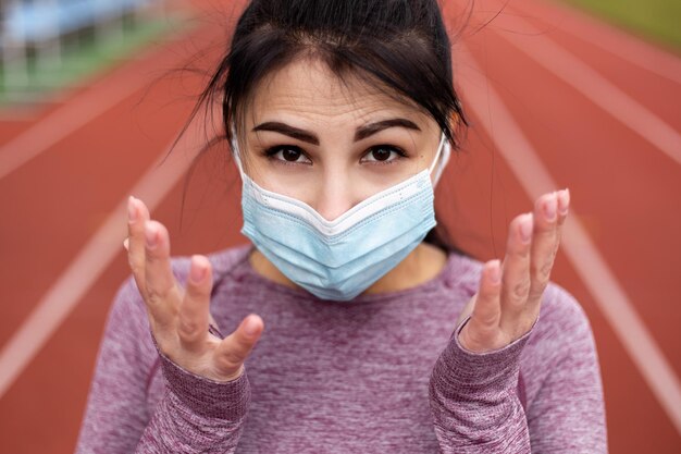 La donna sportiva in tuta sportiva indossa la maschera per il viso sul tapis roulant dello stadio