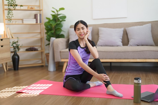 La donna sportiva si siede sulla stuoia di yoga e sorride dopo aver guardato l'allenamento di yoga online per esercitarsi a casa