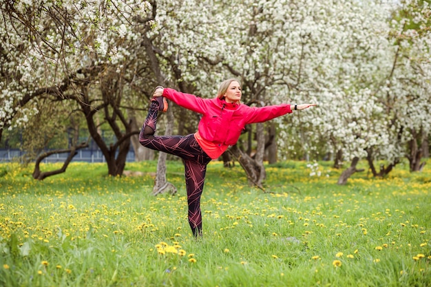 La donna sportiva sta praticando l'yoga all'aperto nel parco in primavera.