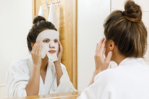 La donna sta applicando la maschera di foglio sul viso