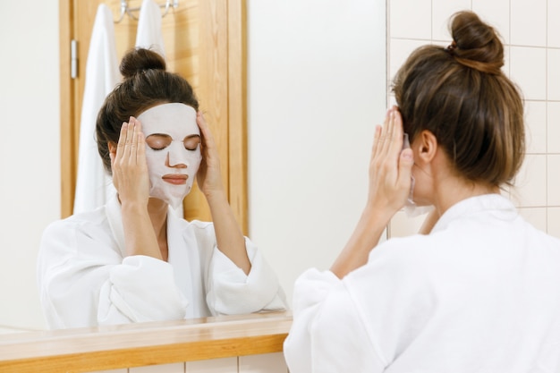 La donna sta applicando la maschera di foglio sul viso