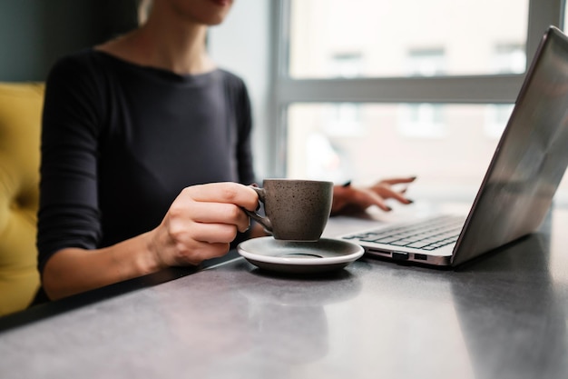 La donna sta bevendo caffè e sta scrivendo su un computer portatile Il concetto di lavoro d'ufficio in un caffè