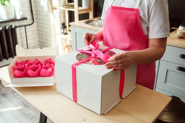 La donna sta confezionando una grande torta di compleanno in una scatola di cupcakes rosa nella confezione sulla scatola