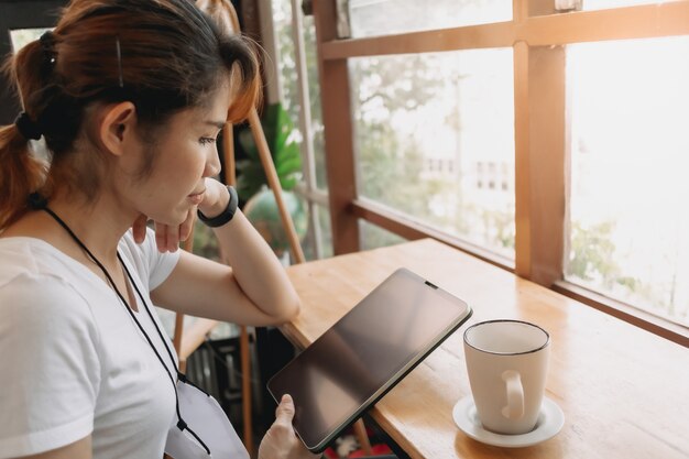 La donna sta guardando il tablet e bevendo caffè al bar