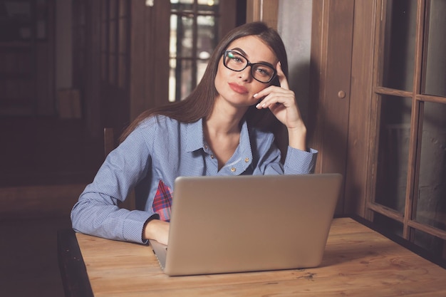 La donna sta lavorando su qualcosa al tavolo di legno con un laptop grigio