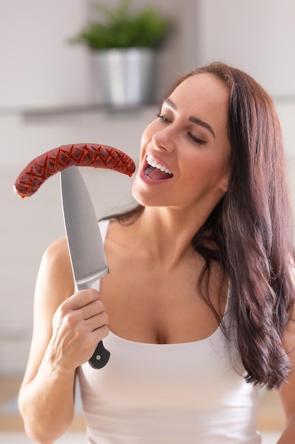 La donna sta per mordere una salsiccia alla griglia pugnalata su un grosso coltello