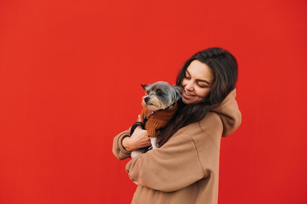 la donna sta su uno sfondo rosso con un cane in braccio e guarda l'animale domestico con un sorriso sul viso