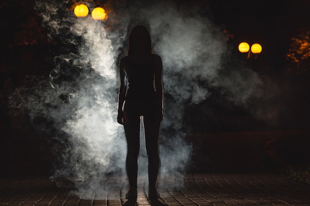 La donna sta sulla strada buia sullo sfondo dei fumi. notte