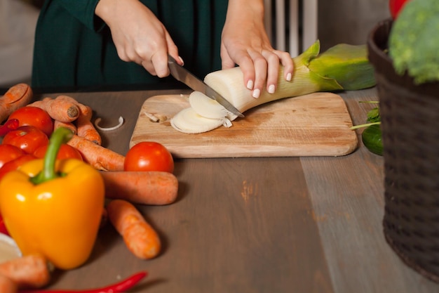 La donna sta tagliando una cipolla con il coltello a tavola con molte verdure