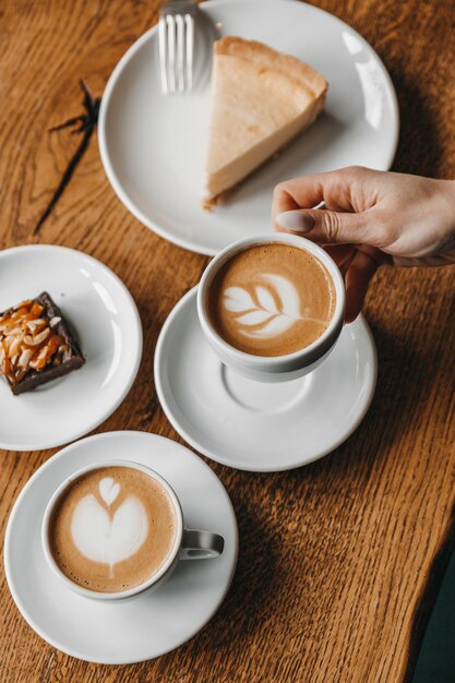 La donna sta tenendo una tazza di caffè vicino alla torta di formaggio e al biscotto posto su un tavolo di legno